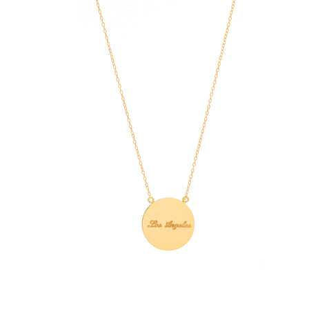 A flat circular gold pendant with inscription with scalloped edges on a gold chain