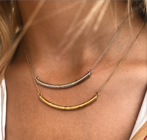 A long gold curved horizontal pendant with inscription on a gold chain