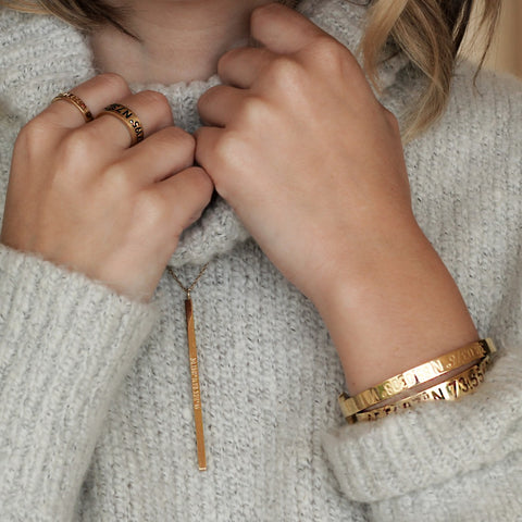 A long slender vertical gold pendant with inscription on a gold chain